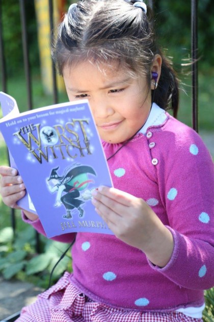 Young girl sitting outside reading a book.