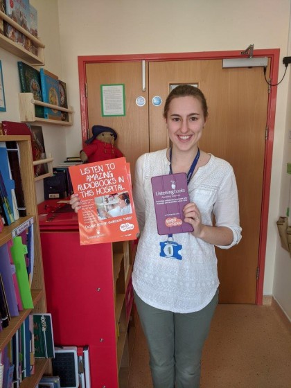 Woman standing in front of a door holding up a Listening Books tablet with a purple case and an orange poster.