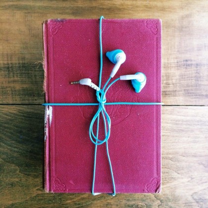 A purple hardback book wrapped with a bow made from earphones, set against a wooden background.