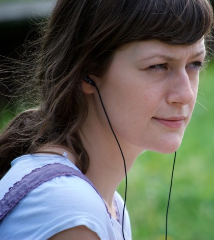 Woman sat outside, listening to a book using headphones.