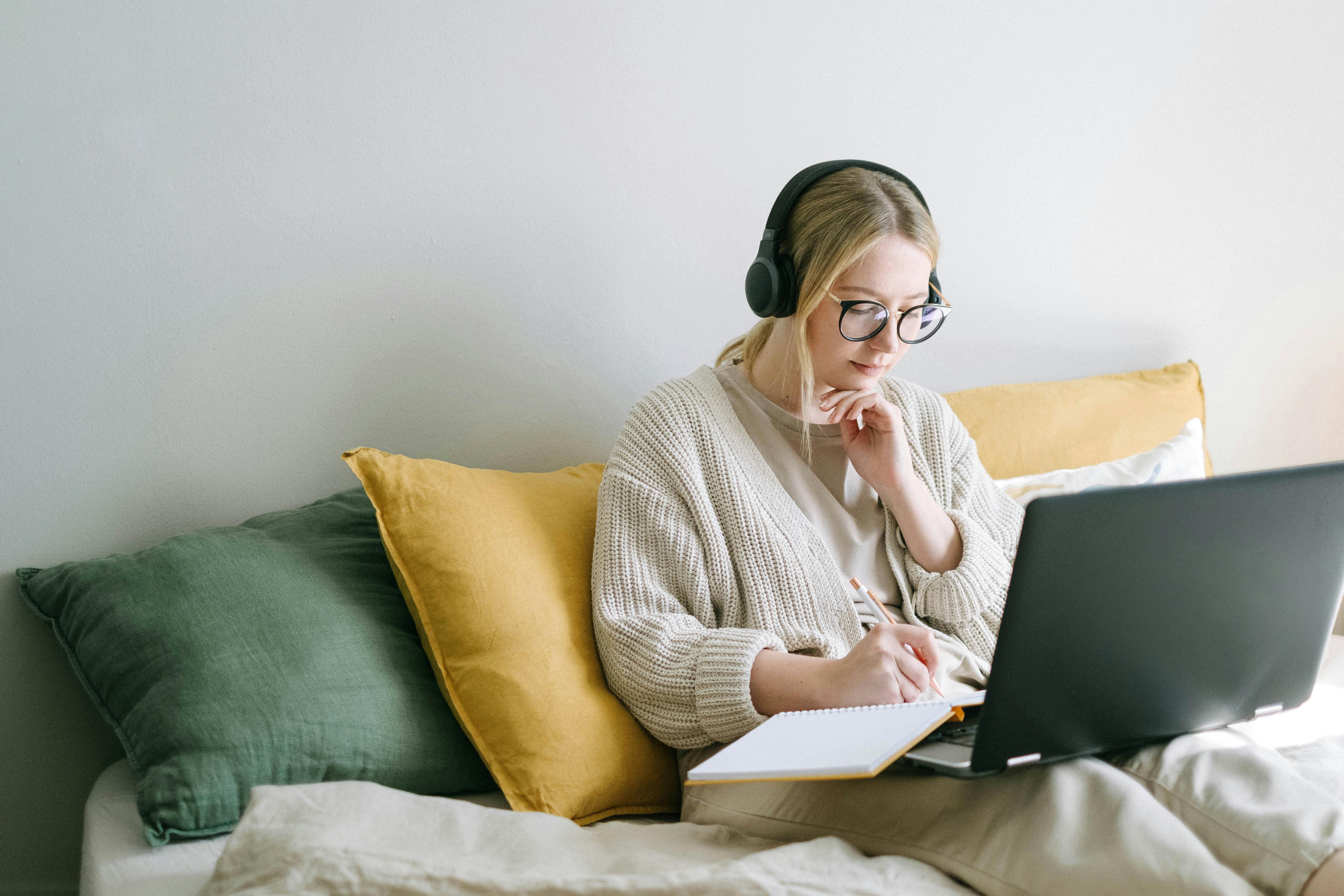 A teen female sitting on the sofa with a laptop on her laps and headphones on