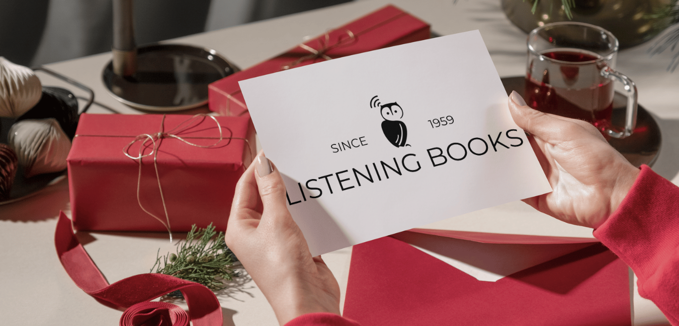 Hands holding a card with Listening Books logo, surrounded by red Christmas presents and Christmas drinks.