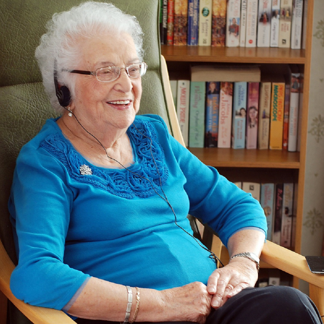 Woman sat in a chair smiling while listening to an audiobook.